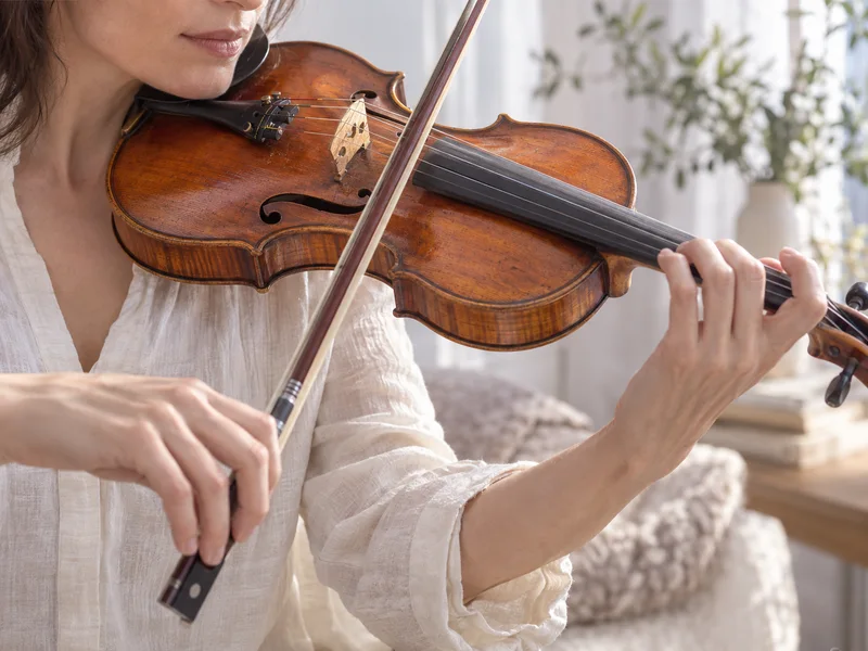 A violinist drawing a bow across the strings of a wooden violin.